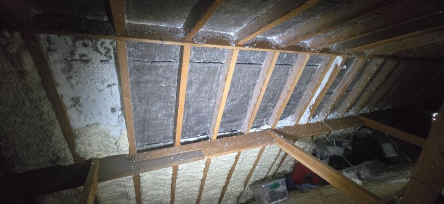 Spray foam insulation removal in progress on a UK roof, rafters exposed